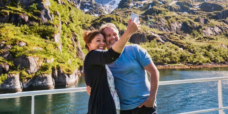 Man en vrouw maken een selfie aan boord van een Hurtigruten schip tijdens een reis met Nordic.