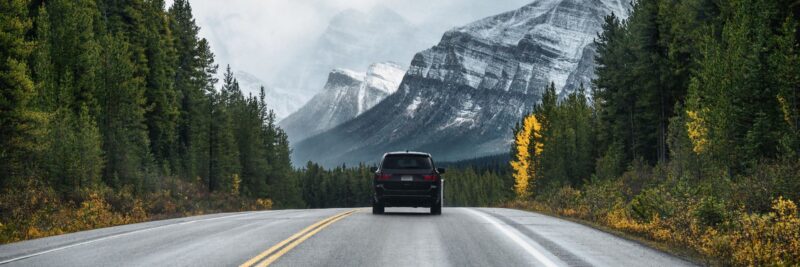 Een auto rijdt door de bossen een bergachtig gebied tegemoet in Scandinavië