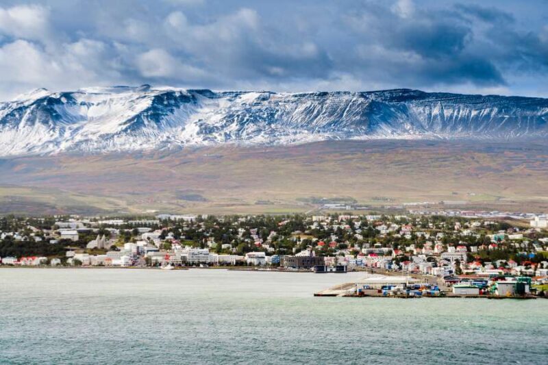 Panoramisch uitzicht op de stad Akureyri in IJsland, gelegen aan de kust met op de achtergrond imposante bergen bedekt met sneeuw. De stad is omringd door groen en kleurrijke gebouwen, met de oceaan op de voorgrond