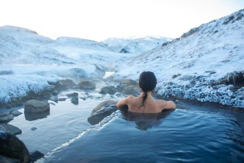 Vrouw die baadt in een hotspring met uitzicht op besneeuwde bergen in IJsland