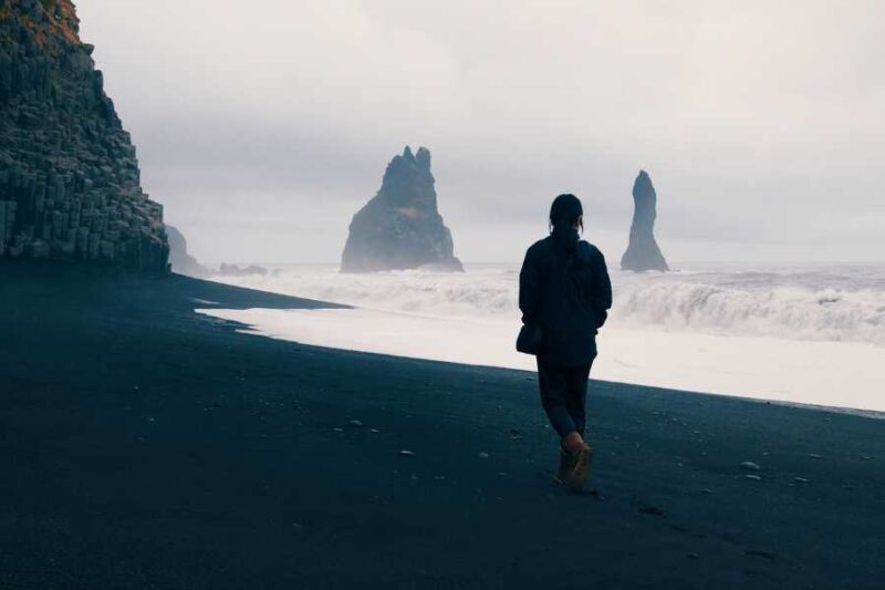 Persoon loopt op een zwart strand in IJsland