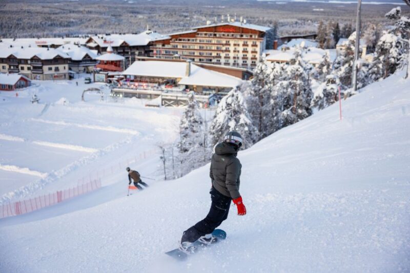 Een snowboarder en skiër die een piste afgaan richting het dorpje Ruka in Fins Lapland.