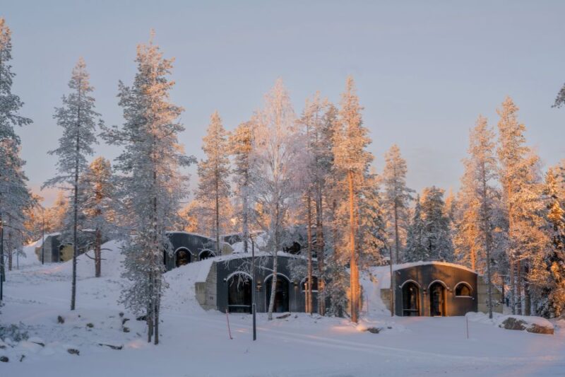 Verschillende cabins van de Kaamos Lodge liggen verscholen onder een laag sneeuw tussen witte bomen.