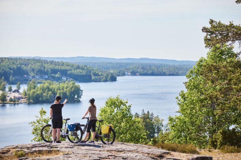 Twee mensen op een fietstocht kijken uit over een meer en uitgestrekte bossen in Dalsland, Zweden.