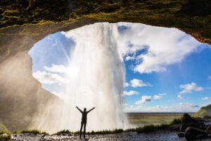 Persoon staat achter de Seljalandsfoss waterval in IJsland met Nordic, de Scandinaviëspecialist