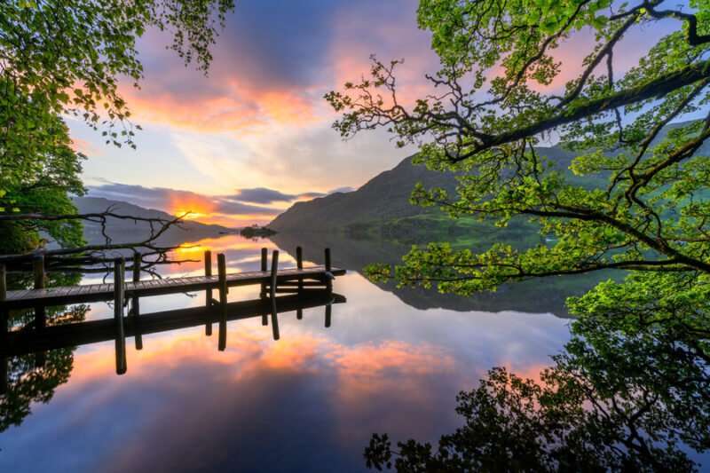 Mooie rustige reflecties in het meer met zomerzonsopgang en oude houten steiger bij Ullswater in The Lake District National Park Engeland